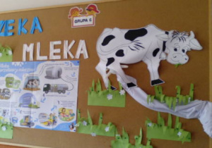Zdjęcie tablicy z napisem "Rzeka mleka" na której widać plakat, krówkę na trawie